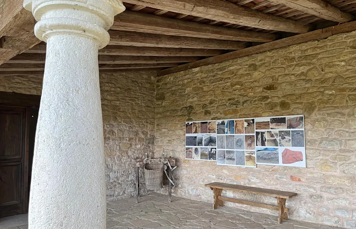 Zu sehen ist eine Säule im Vordergrund und in der Ecke eine Bank sowie Bilder an der Wand. Das Bild gehört zu Apsis an der Stirnseite des Wohnhauses.