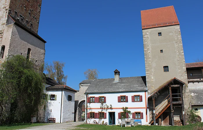 Bauernhof mit weißen Gebäuden, zwei Türmen und Gartenmöbeln unter blauem Himmel.